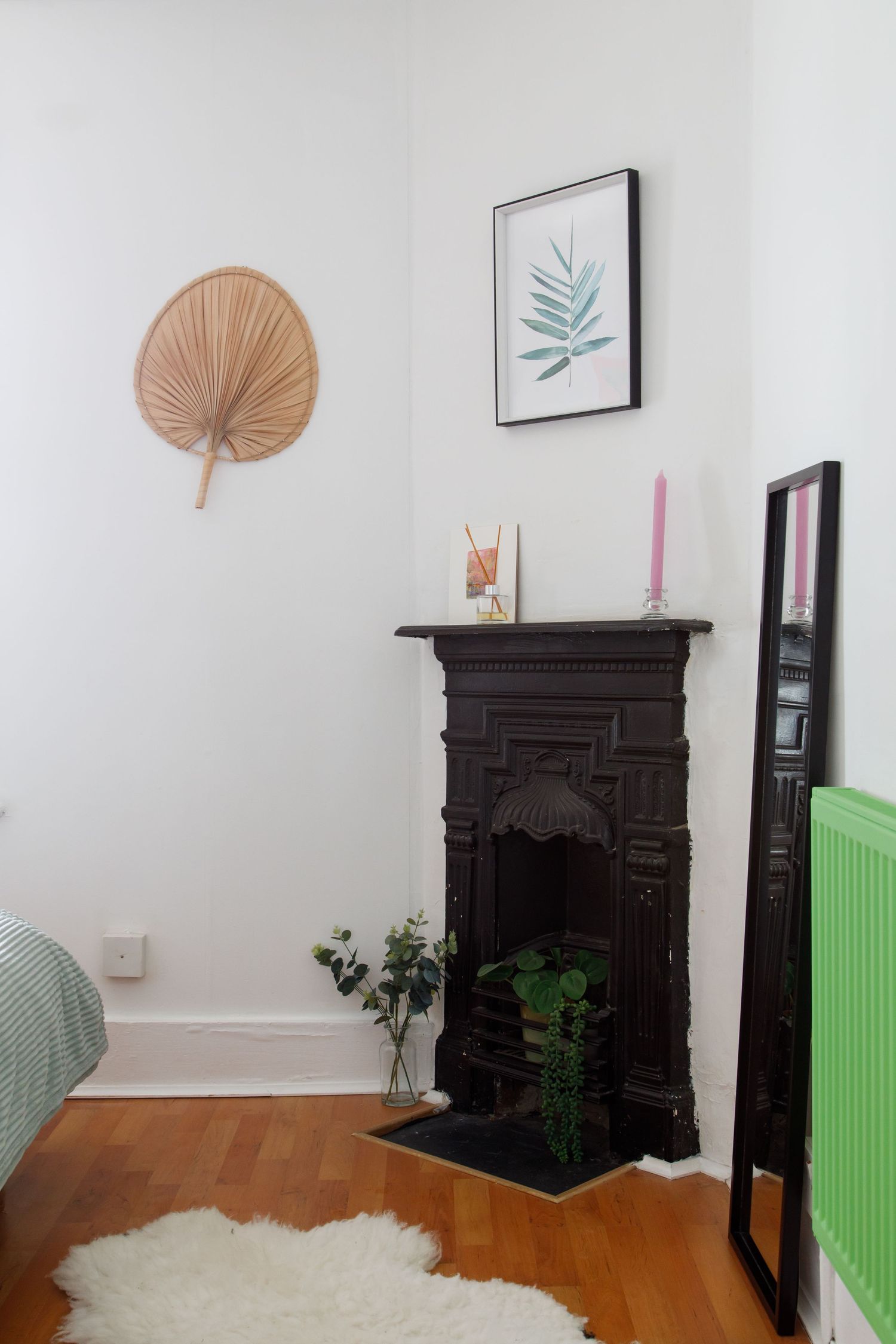 Vintage cast iron fireplace with palm leaf decor and botanical print in white minimalist room taken during an interiors/lifestyle photoshoo.
