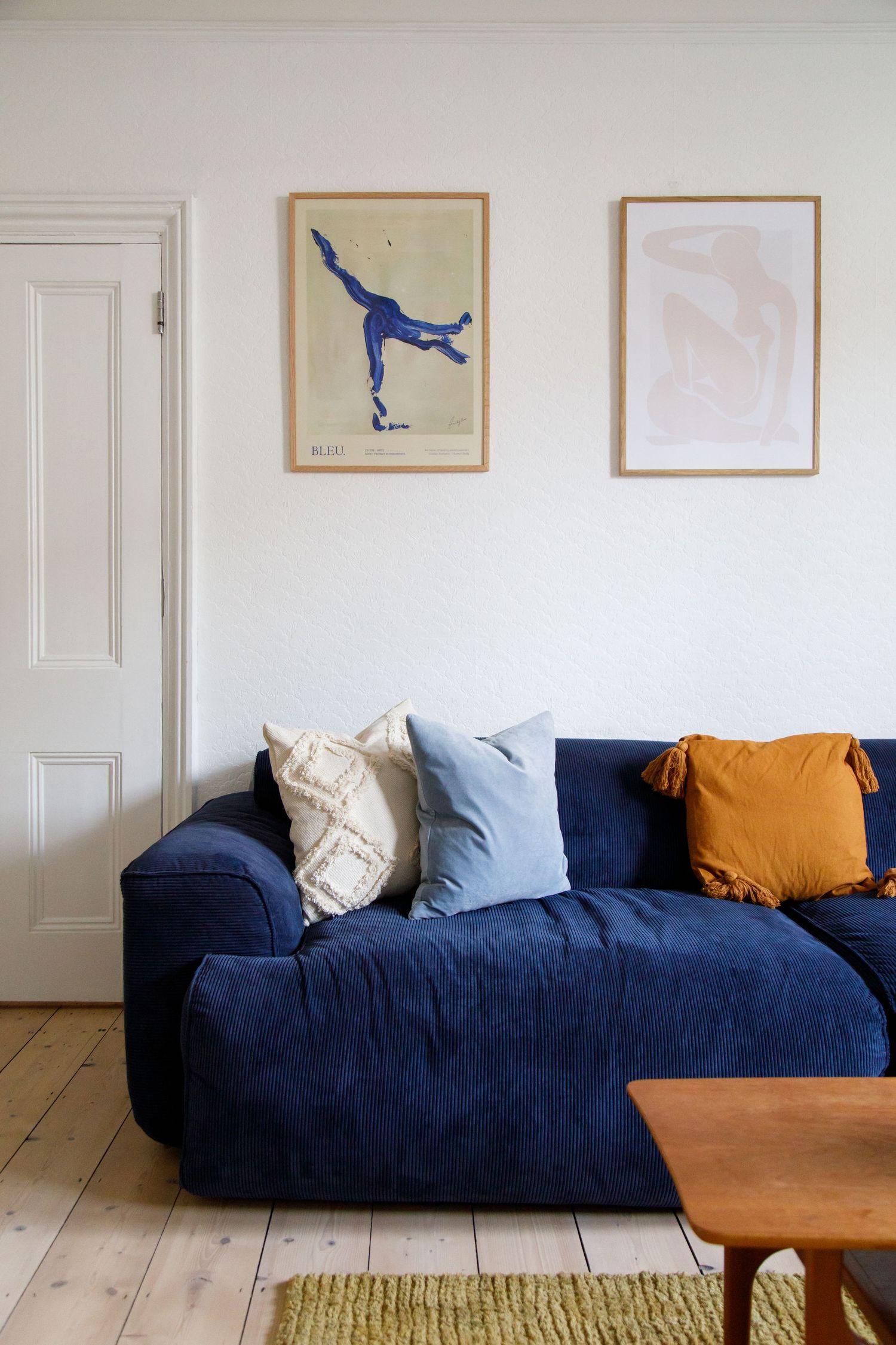 Navy blue sofa with colorful cushions beneath framed figure skating artwork taken during an interiors/lifestyle photoshoot.