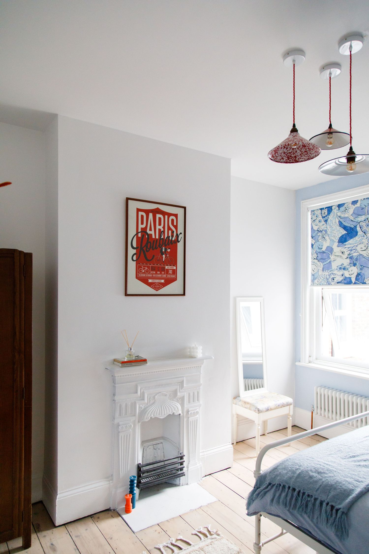 Minimalist bedroom with Paris poster, white fireplace and blue accents taken during an interiors/lifestyle photoshoot.