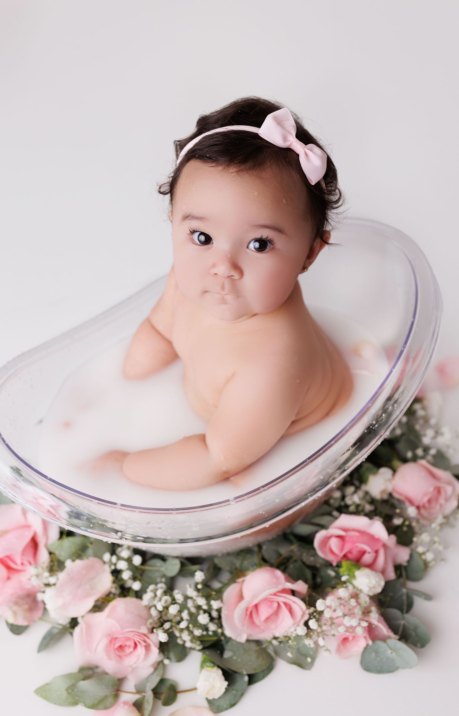 Artistic newborn portraits in milk bath with pink roses and greenery.