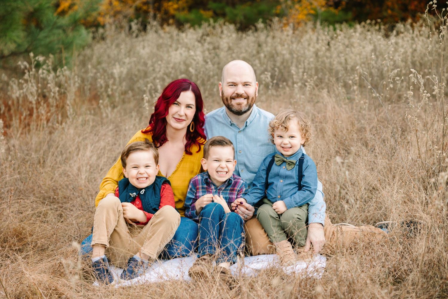 Family sitting together in tall grass with autumn colors in the background.