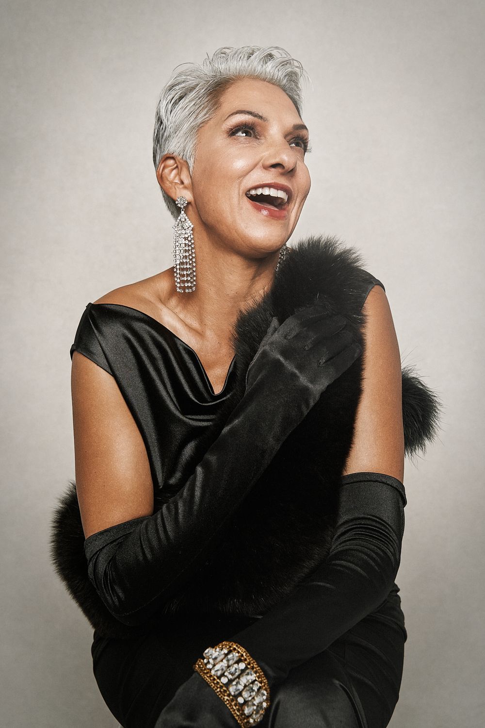 Stylish older woman with short gray hair laughs joyfully wearing a black gown and long gloves.