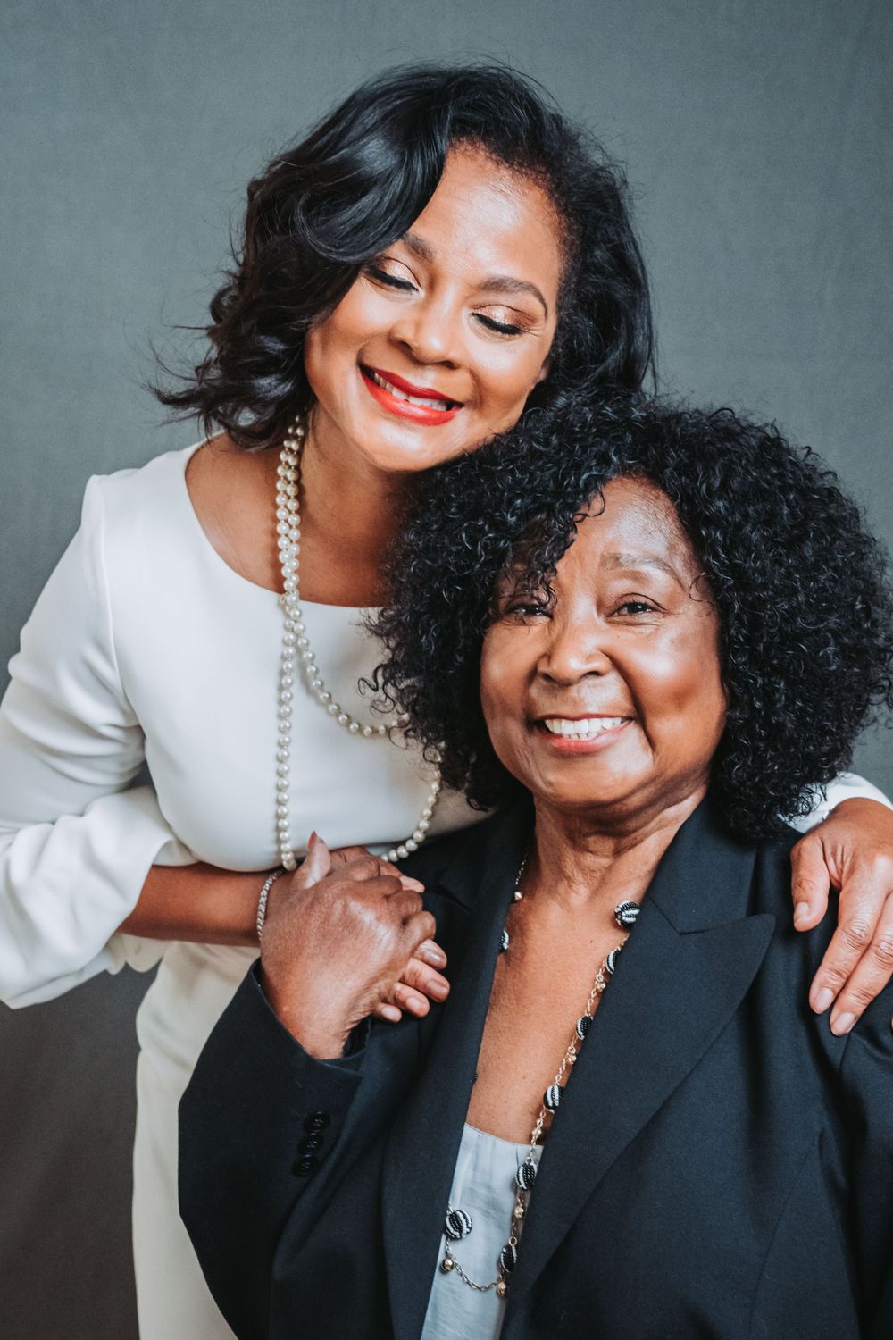 Two smiling women in formal attire posing together in a warm studio portrait.