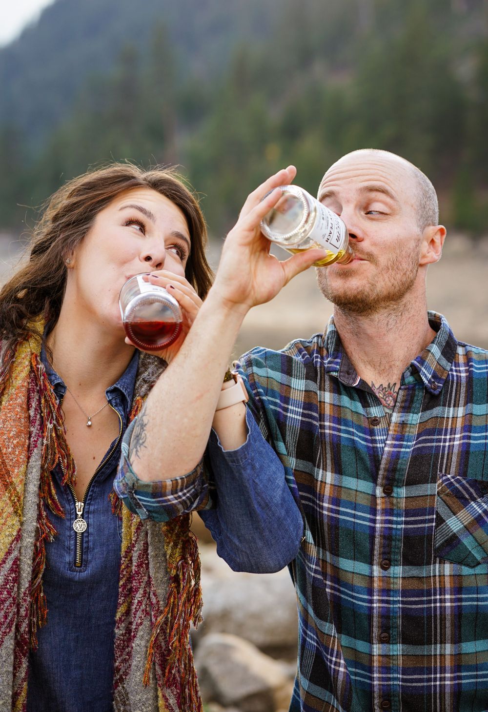 Couple shares drinks and laughter by mountain lake during outdoor adventure.