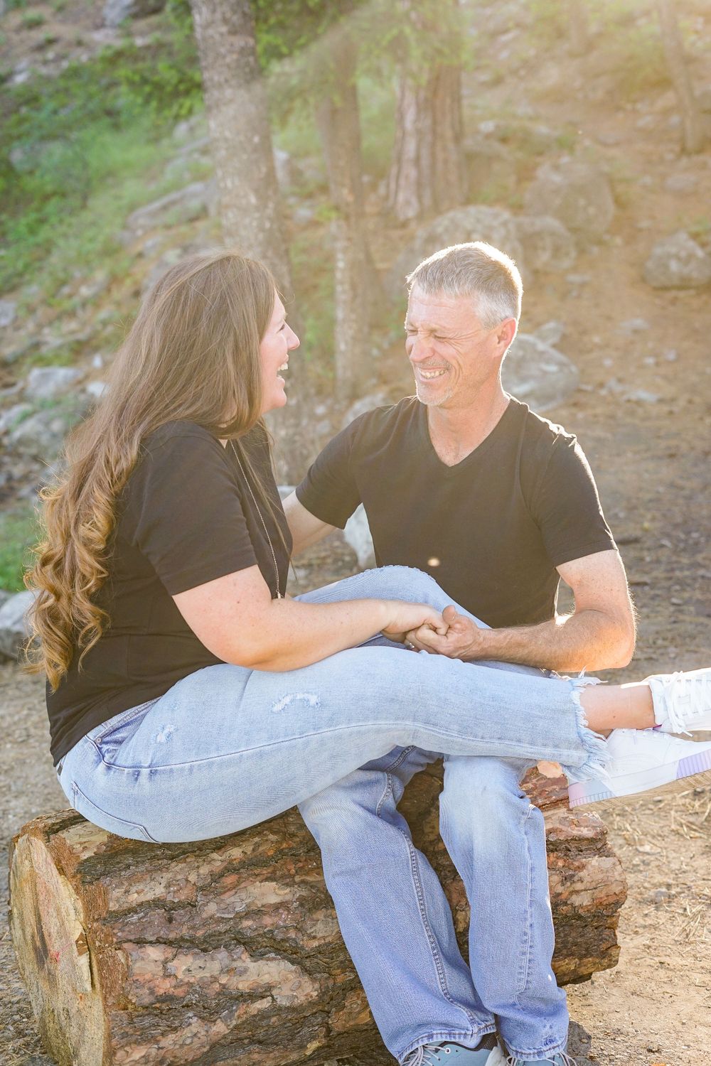 Couple in matching black t-shirts sitting intimately on a log in a natural outdoor setting.