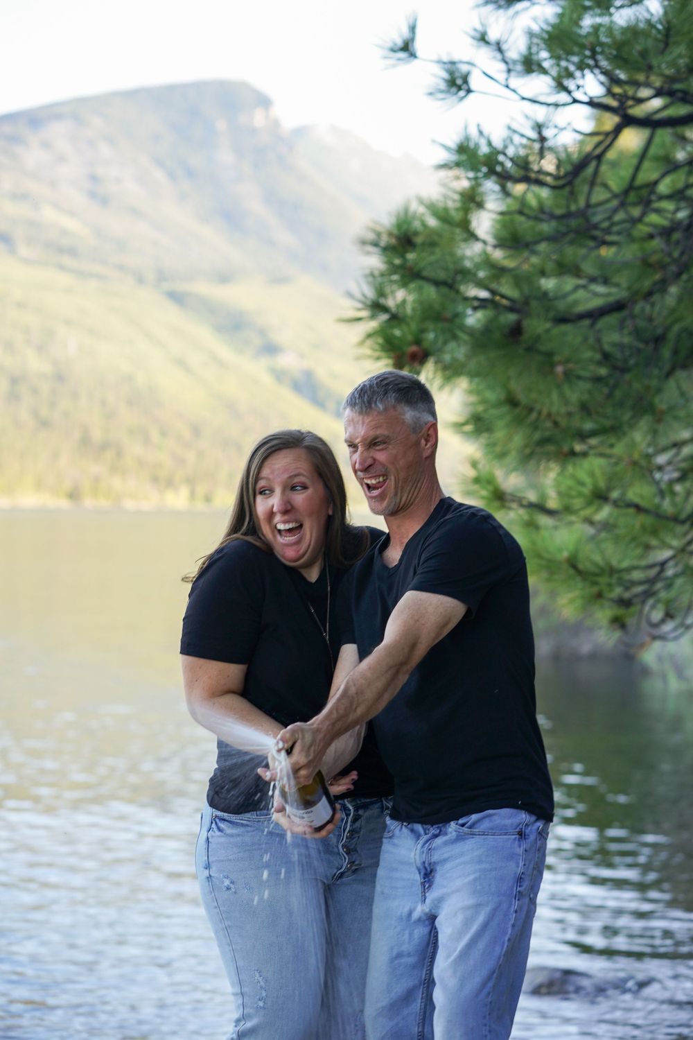 Joyful couple sharing a playful moment by a mountain lake on a sunny day.