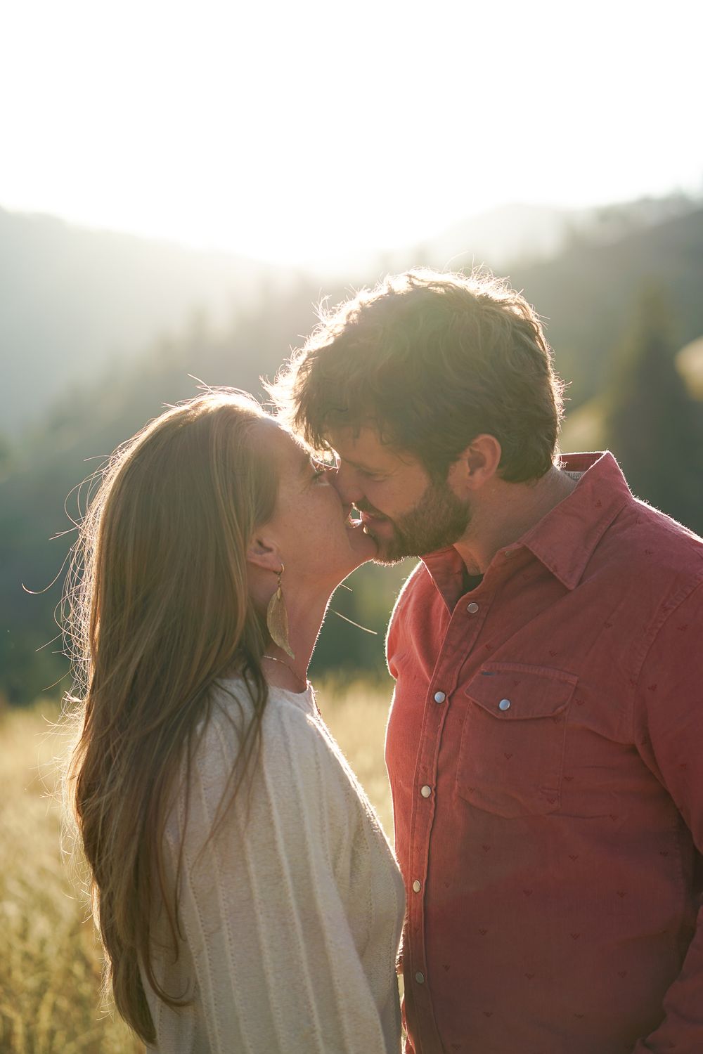 An intimate moment shared between a couple in a sunlit meadow with mountains behind.