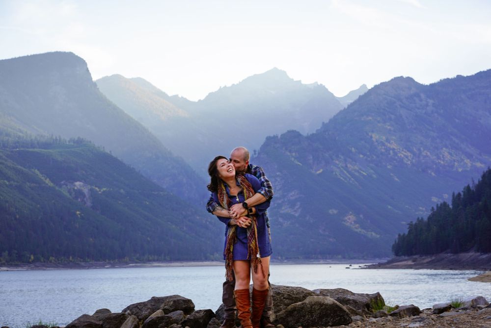 Silhouetted couple embraces against dramatic mountain lake landscape.