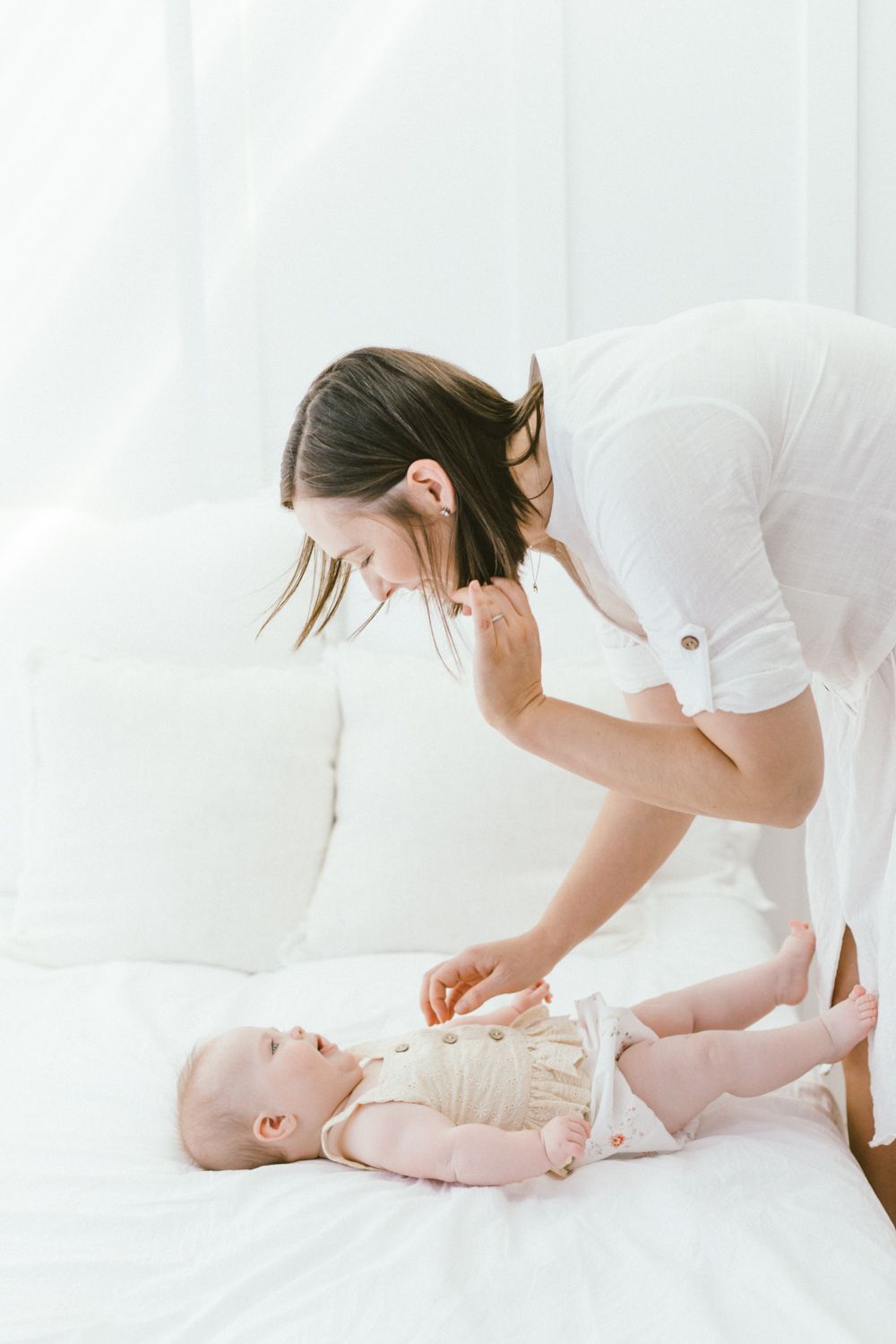 Caregiver in white shirt playing with baby on white sofa.