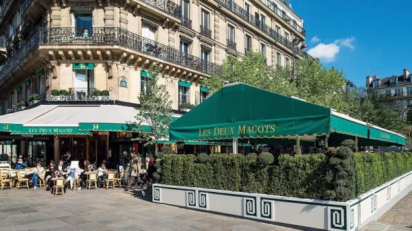 Famous Parisian cafe with green awnings and outdoor seating along a classic Haussmann-style building.