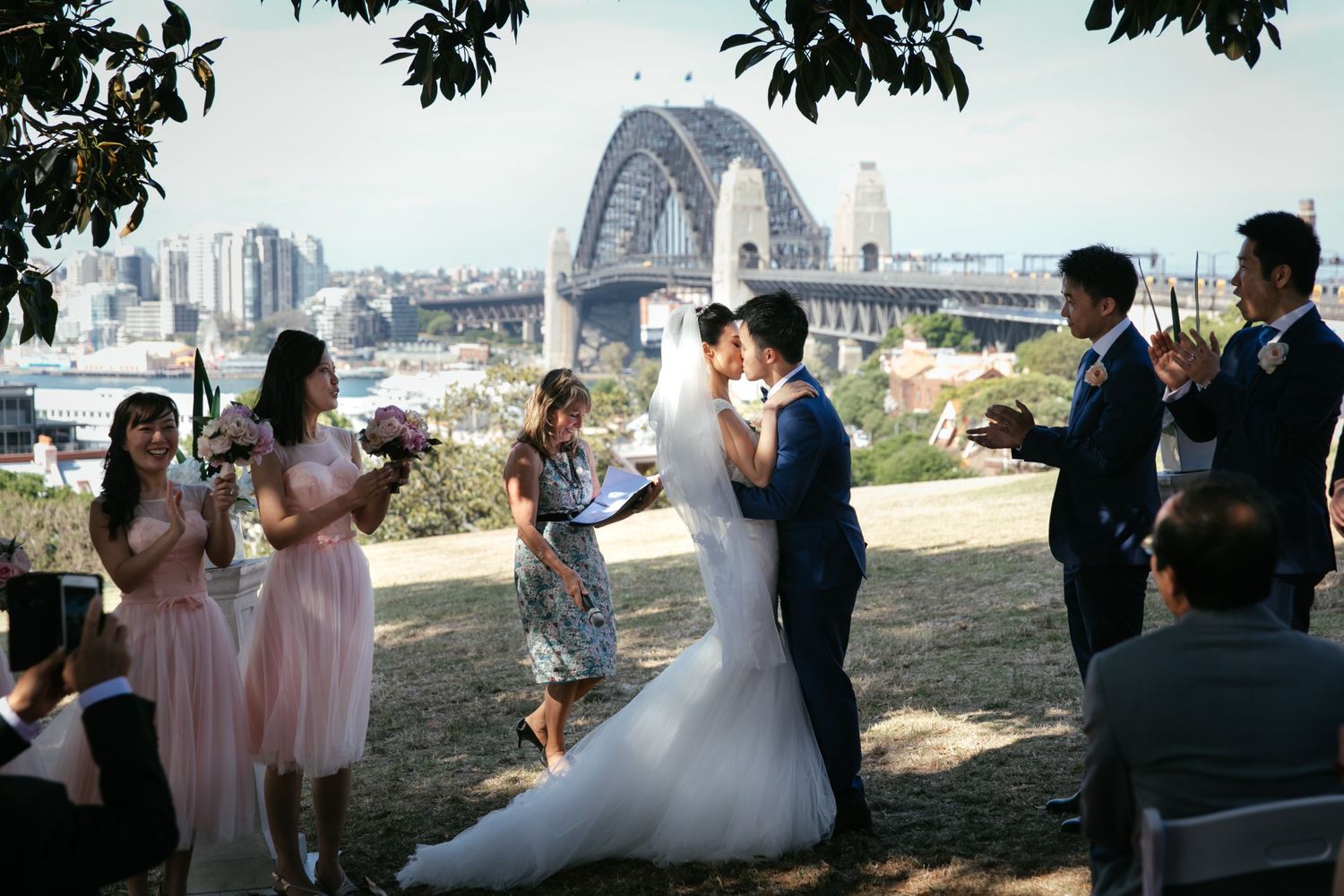 Couple shares first kiss at outdoor wedding with Sydney Harbour Bridge backdrop.