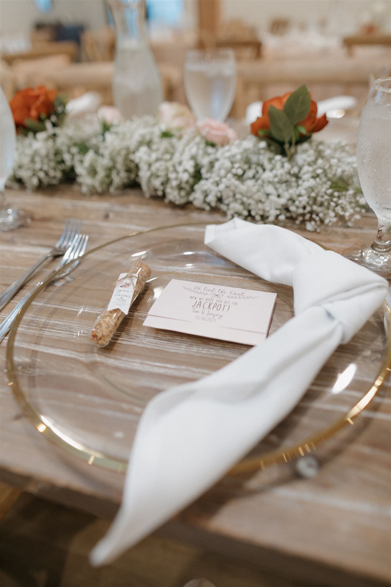 Elegant place setting with clear charger plate, white napkin, and floral accents.