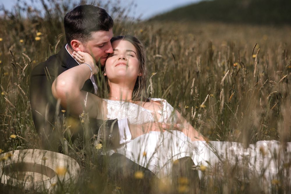A couple shares an intimate moment among tall grass in a summer field.