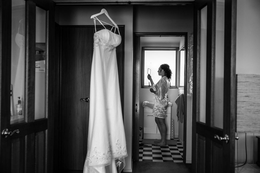 A wedding dress hangs in a hallway while a figure stands in silhouette by a window.