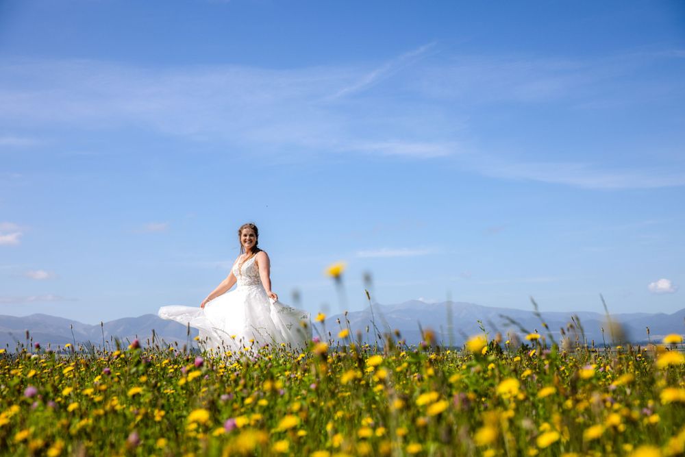 A figure in a white wedding dress stands in a field of yellow wildflowers against blue sky.