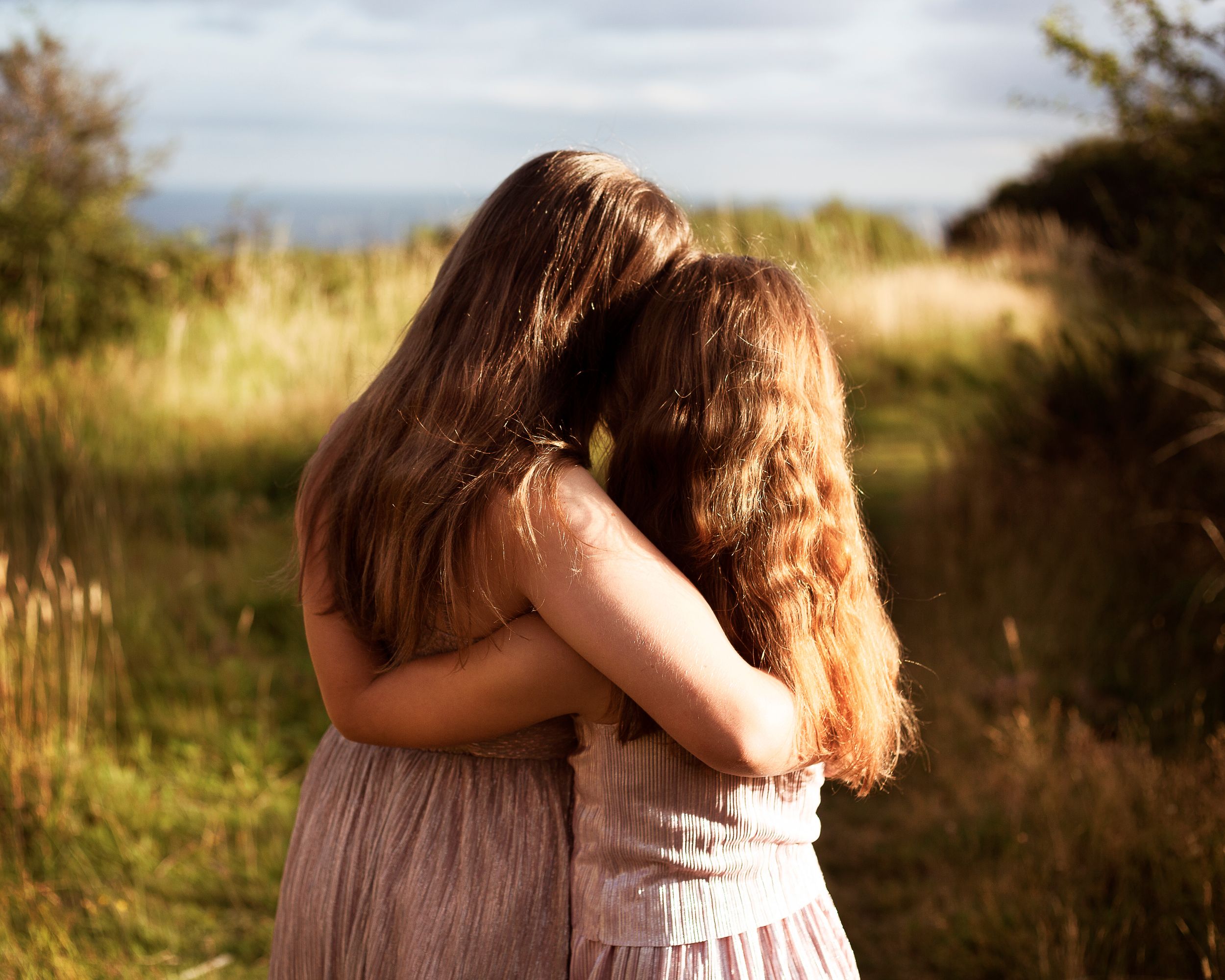 Back shot of two young sisters cuddling on a cliff top in golden light