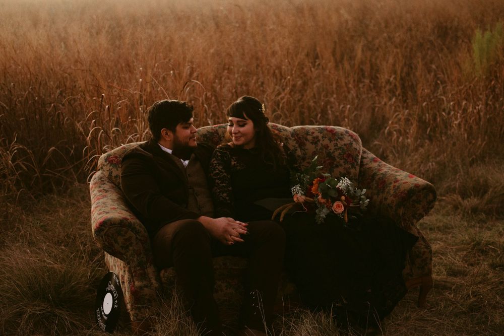 Two people in dark formal wear share an intimate conversation on an outdoor sofa.
