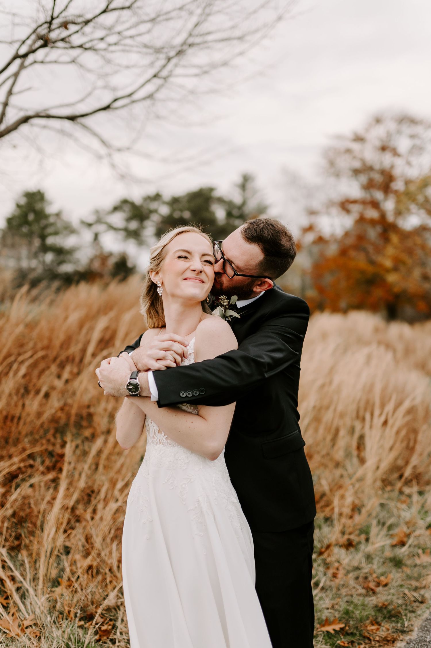 Joyful wedding couple dancing in a field of autumn grass during sunset.