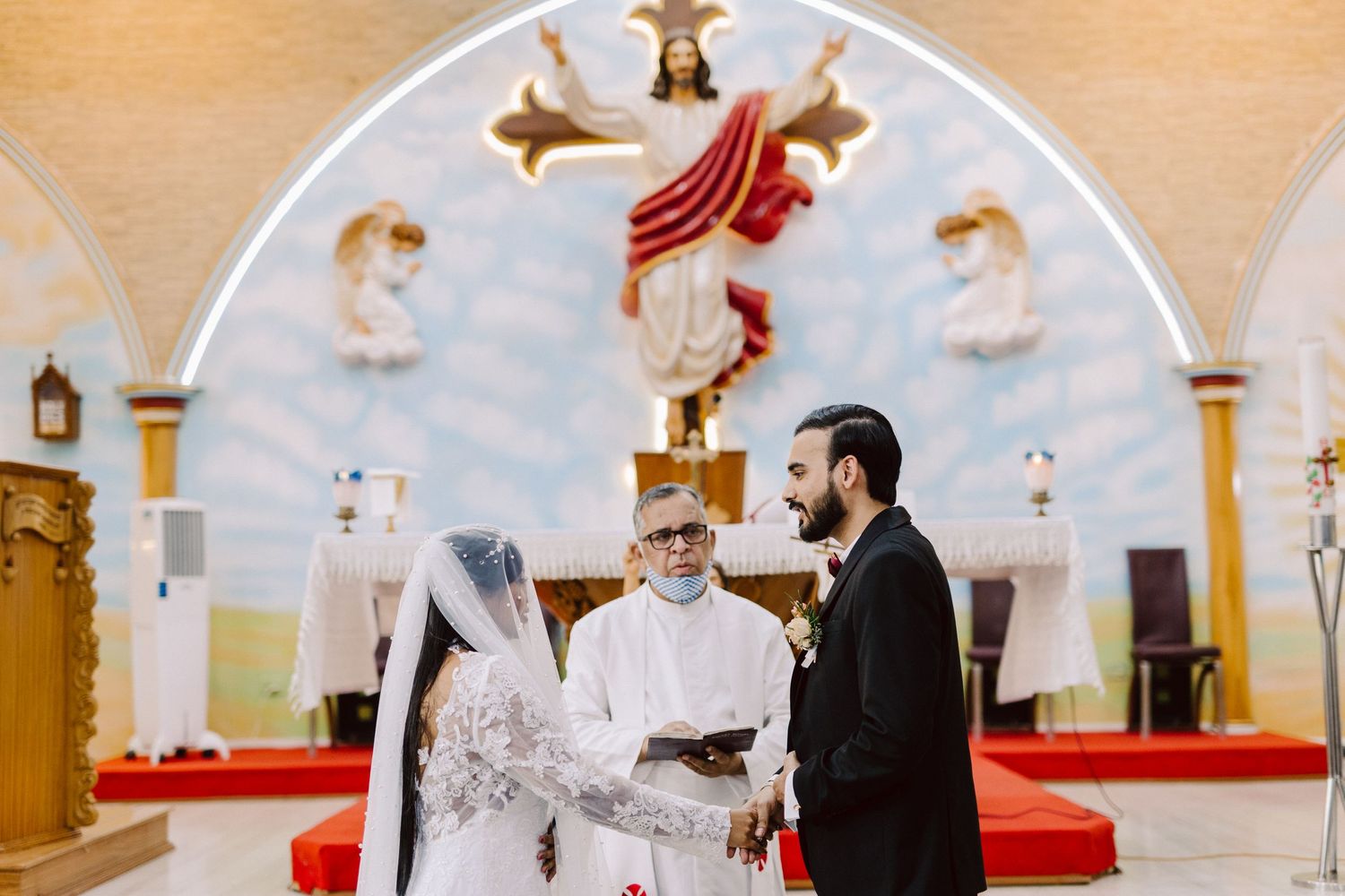 Catholic church wedding ceremony with ornate altar decorations and religious artwork.