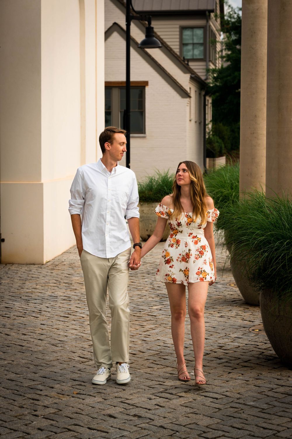Couple strolling together on cobblestone path wearing coordinated white and floral outfits.