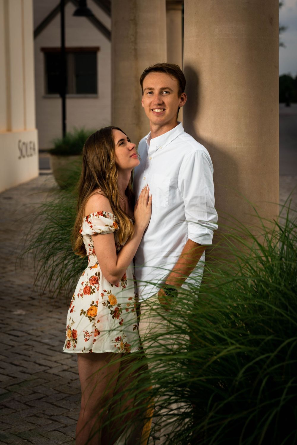 Romantic couple pose by a column in coordinated summer outfits.