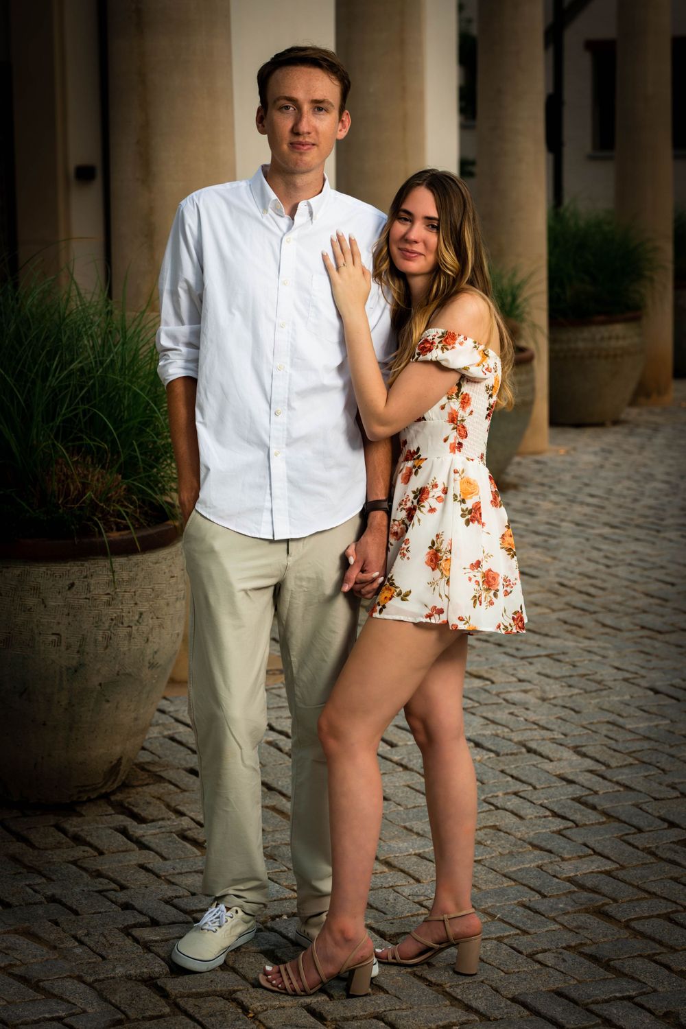 Couple embracing by architectural columns in coordinated white and floral outfits.