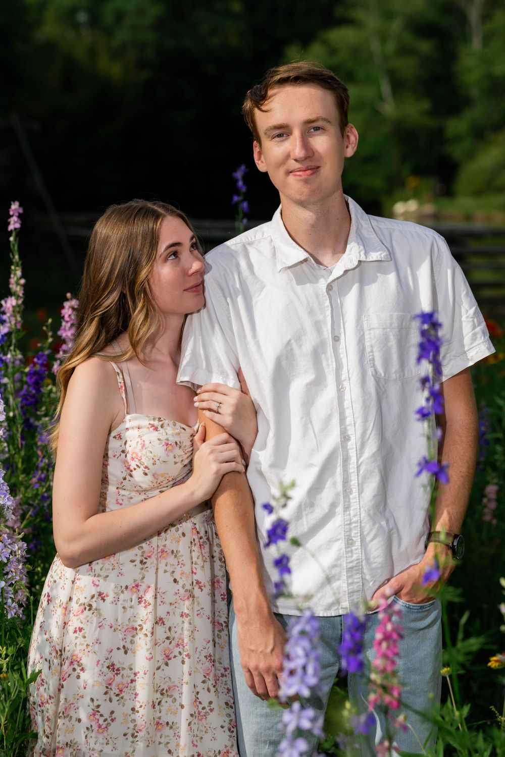 Couple stands together in garden with blooming purple delphiniums.