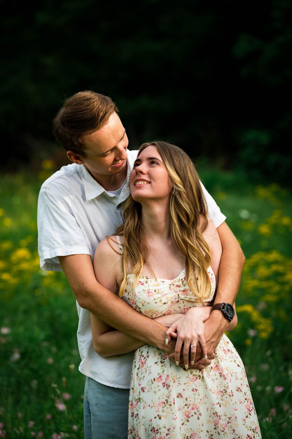 A romantic couple embraces in a field of yellow wildflowers during a sunny summer photoshoot.