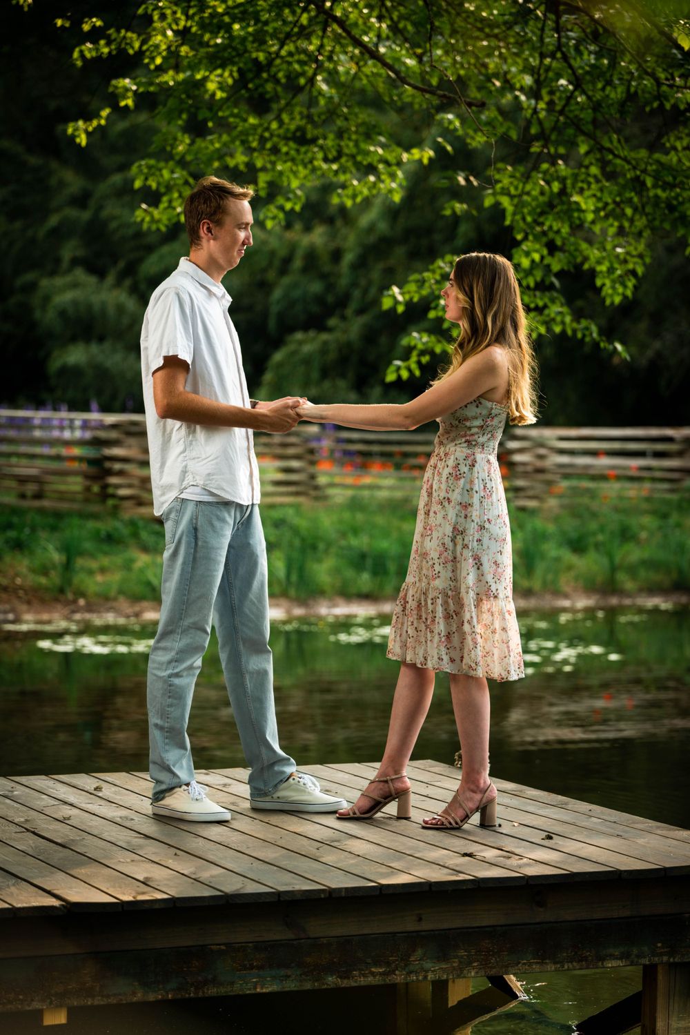 A couple shares tender moments on a wooden dock by a tranquil pond at sunset.