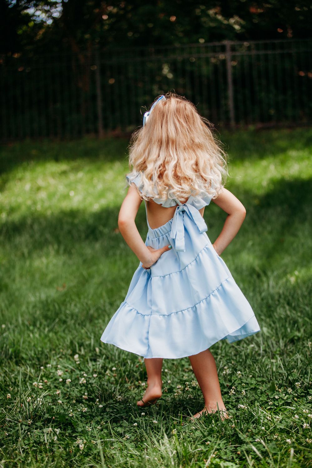 Young child in a blue ruffled dress twirling in a sunny garden.