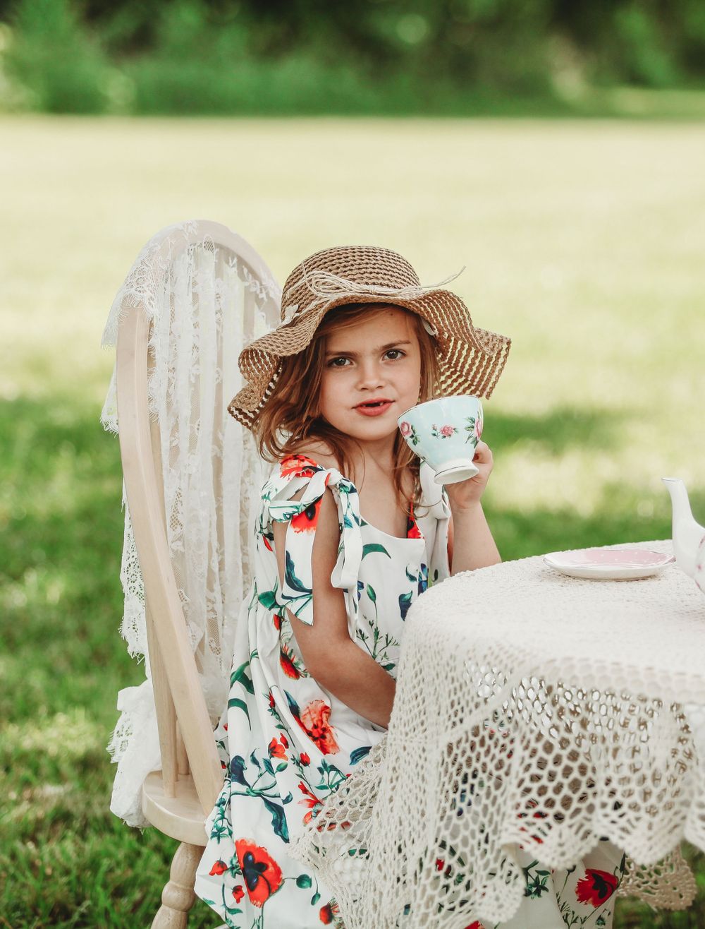 Tea party scene with lace tablecloth and floral dress in sunny garden setting.