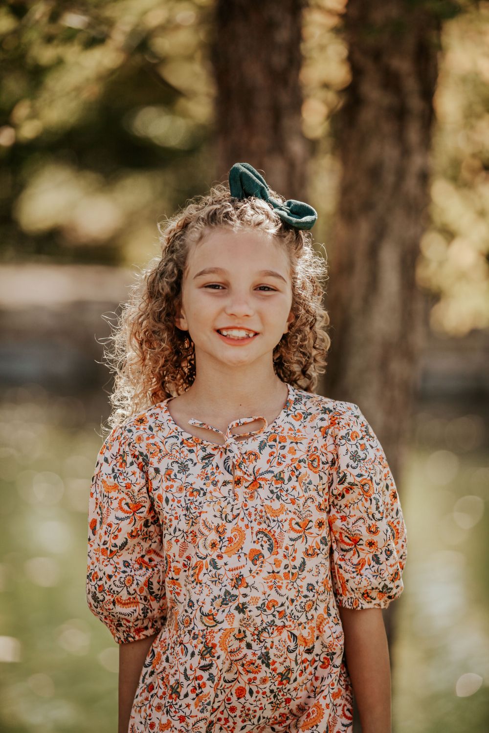 Child in a floral dress smiles during an outdoor photo session.