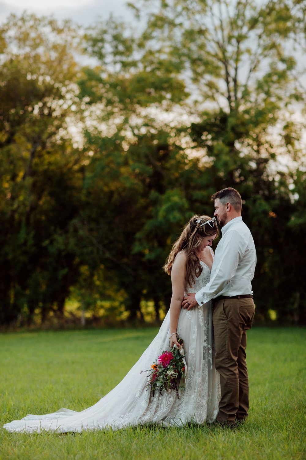 A couple shares an intimate moment at sunset in a field with the bride's lace dress trailing behind.