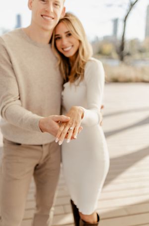 Newly engaged couple in matching beige outfits showing off ring.