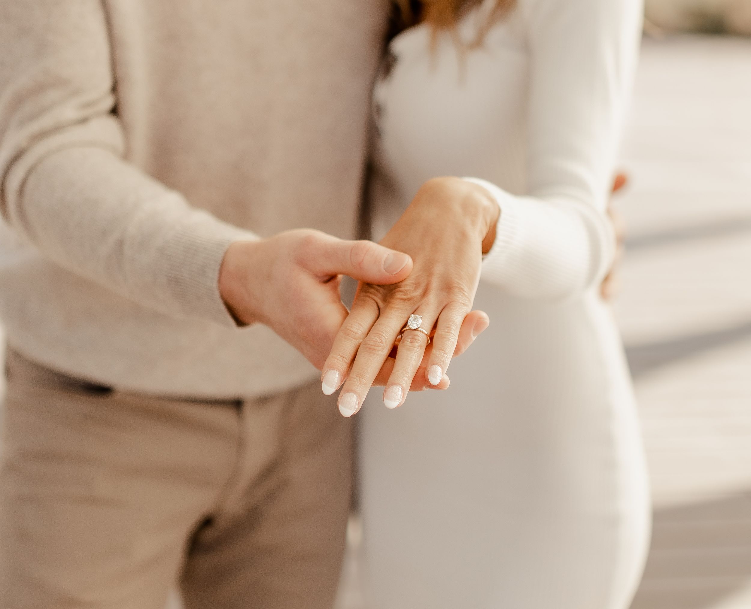 Close-up of hands showing engagement ring with neutral toned clothing.