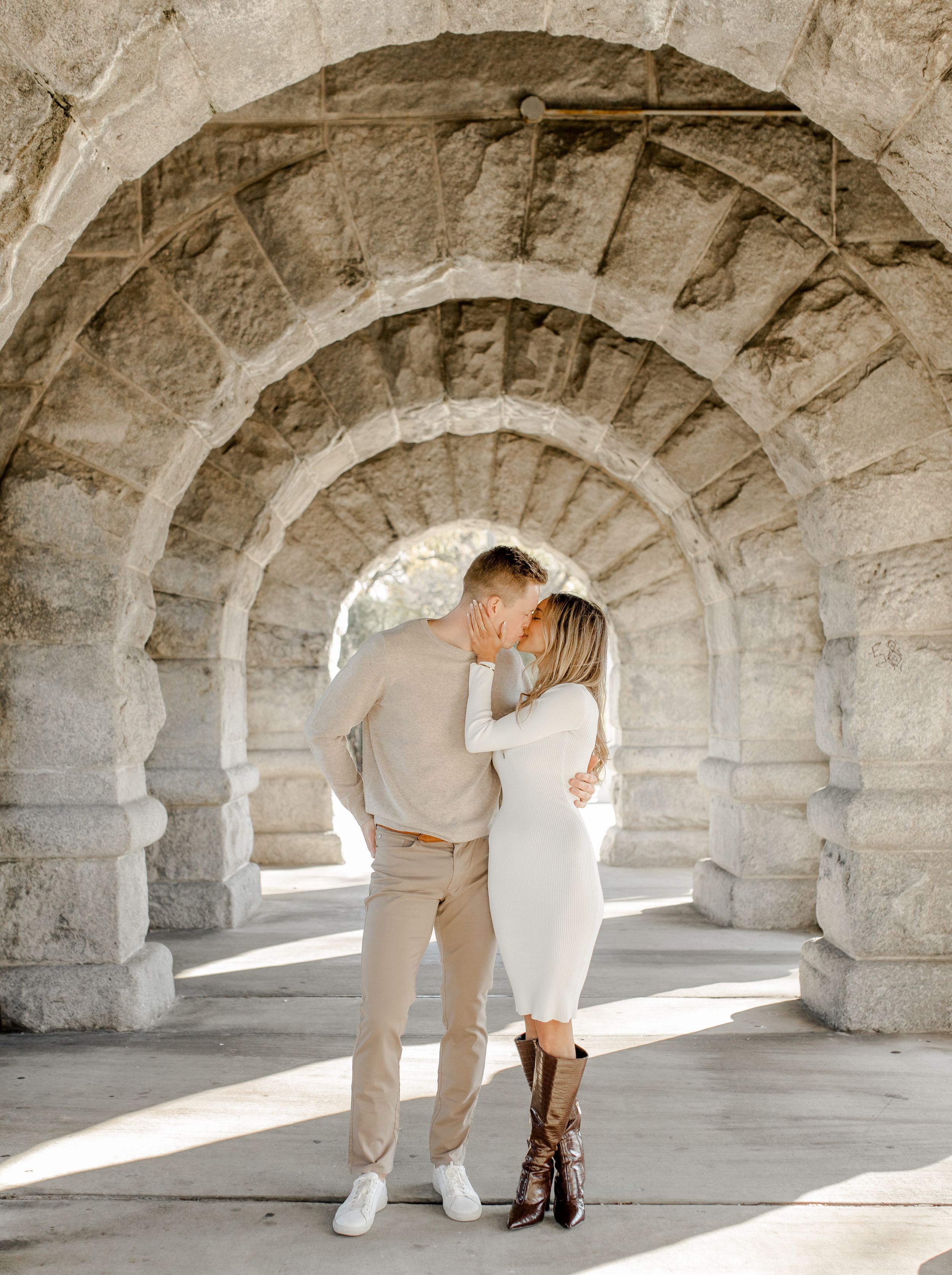 Couple sharing an intimate moment in stone archway tunnel with sunlight streaming through.