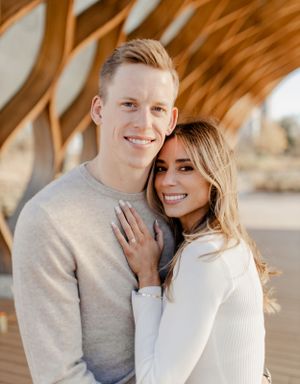 Romantic couple in neutral sweaters embracing under a wooden architectural structure.