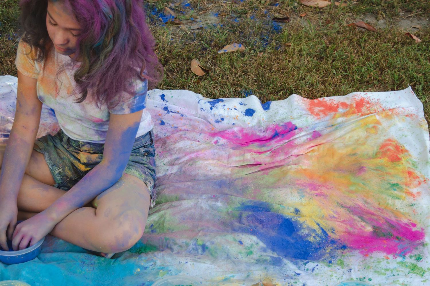 Artist sits on ground with colorful tie-dye artwork spread out on fabric.
