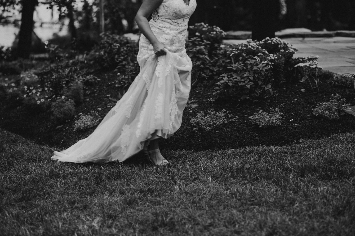 black and white artistic image focusing on a bride's dress and shoes as she runs through wet grass