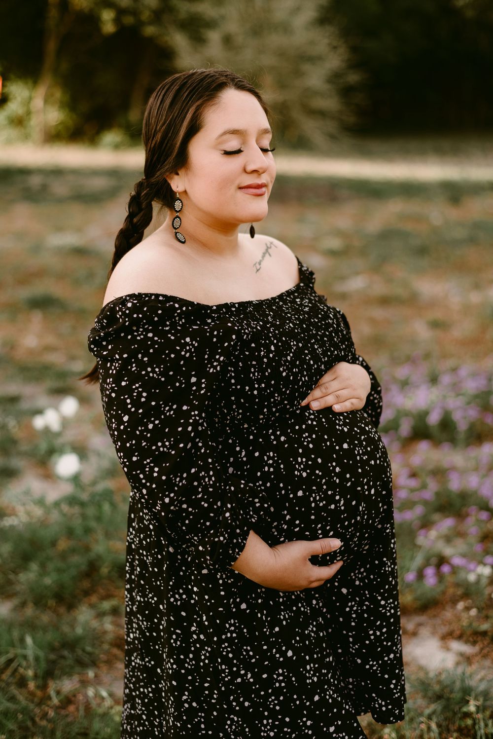 Serene maternity portrait in a sparkly black dress with wildflowers in background.