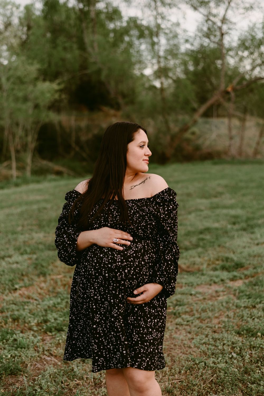 A side-view maternity portrait in a natural setting with long dark hair and a patterned dress.