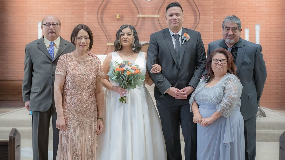 Wedding party group portrait with bride, groom, and four family members inside a church ceremony.