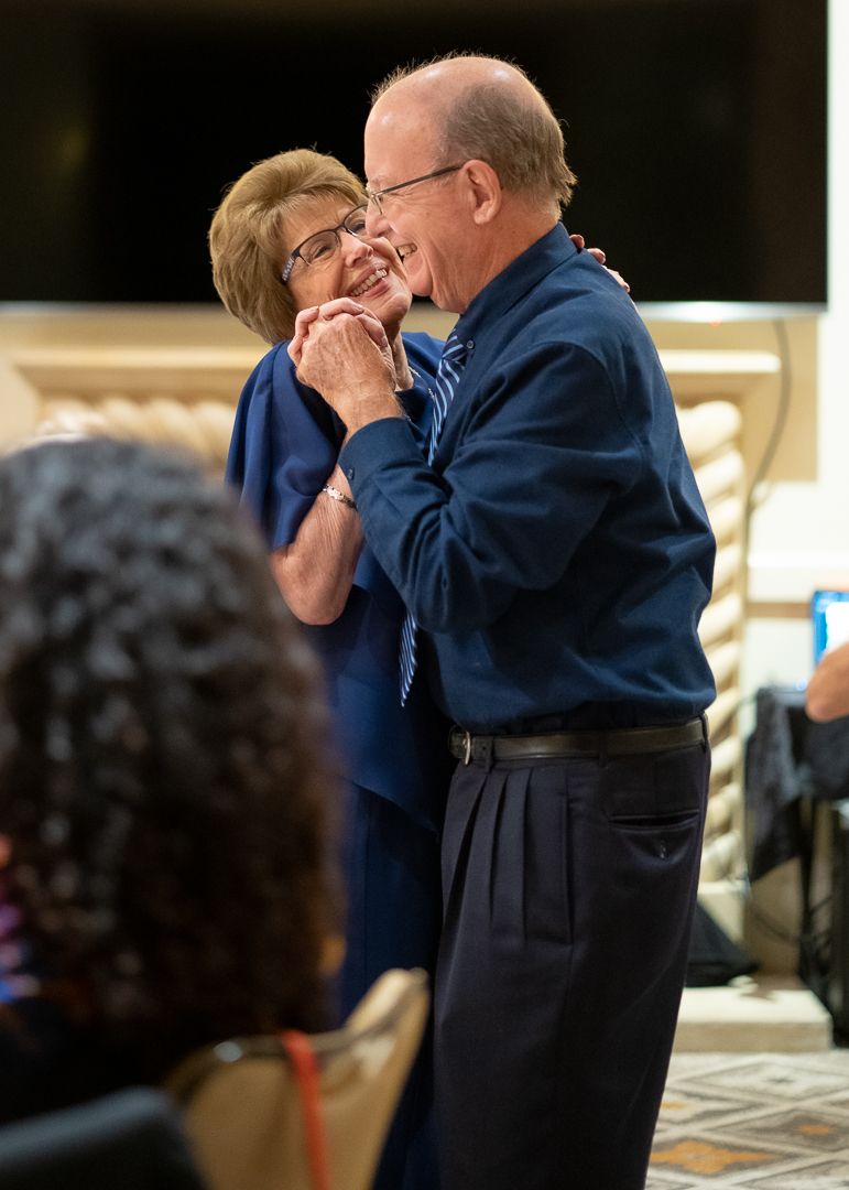 Older couple slow dancing and smiling tenderly at an indoor celebration or anniversary party.