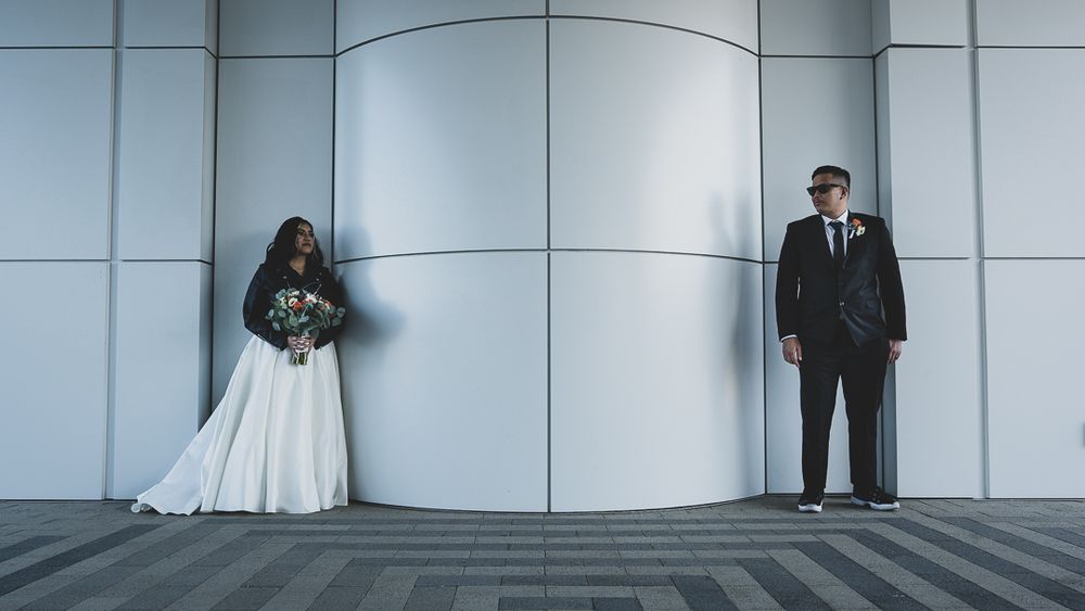 Bride and groom stand apart against a modern gray wall in an artistic wedding portrait.