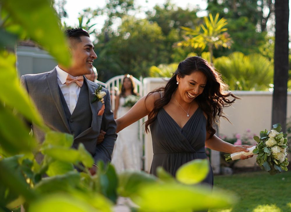 Smiling couple in wedding attire walking through a lush garden during an outdoor wedding ceremony.