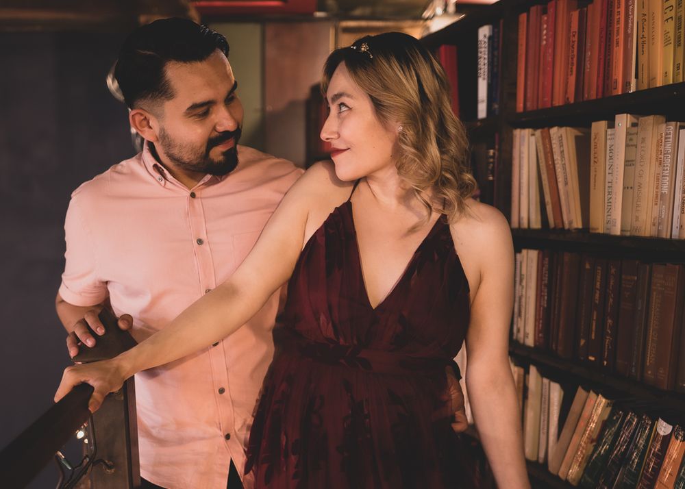 Stylish couple sharing a playful moment together beside bookshelves in a cozy library setting.