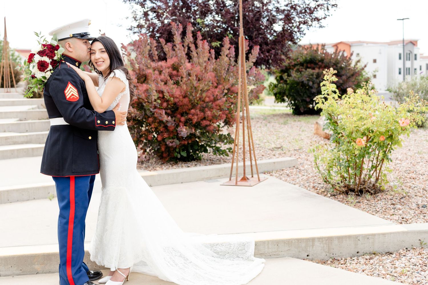 Military wedding couple embraces near autumn foliage and steps.