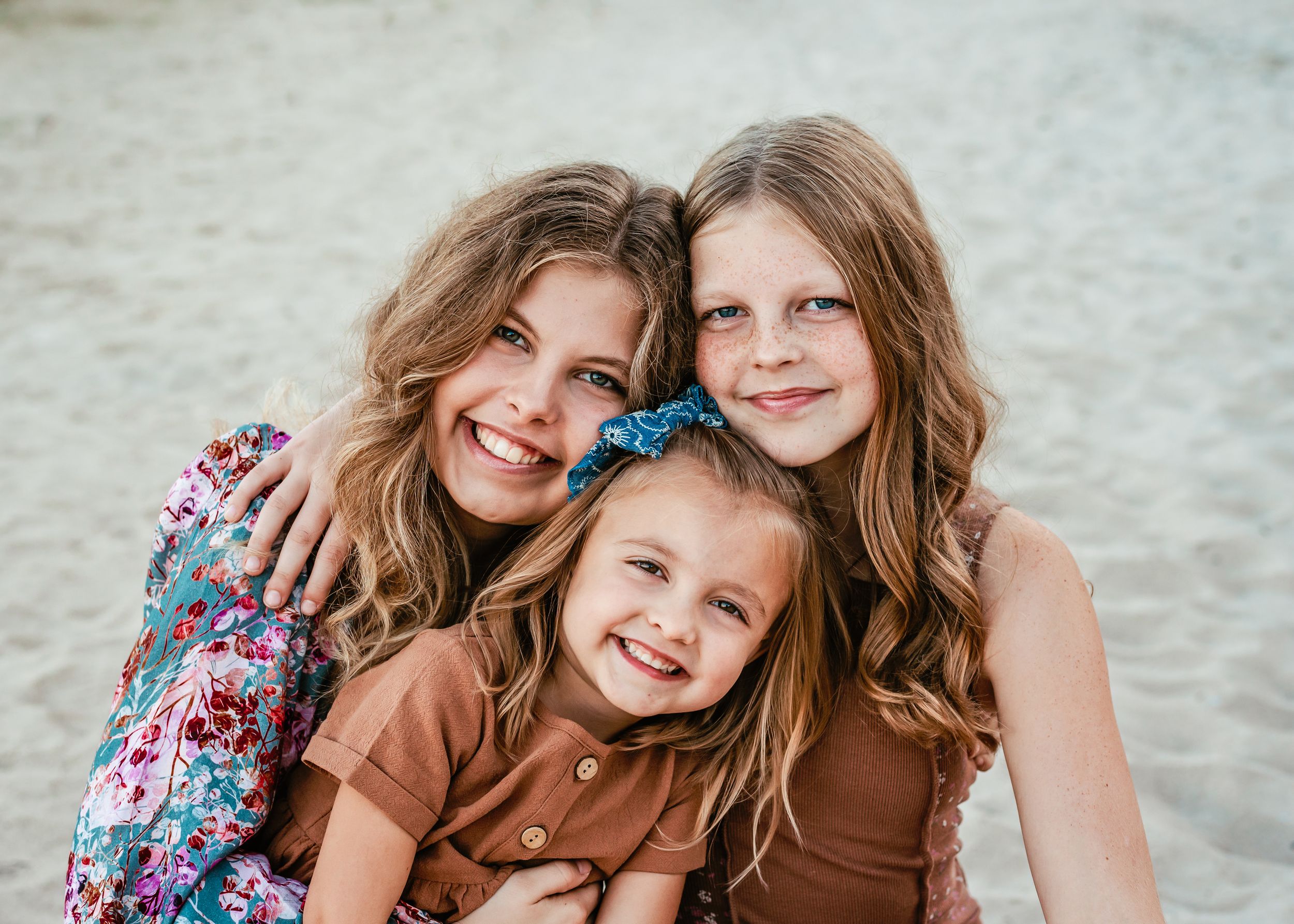 Three people with long hair share a close, joyful moment on the beach.