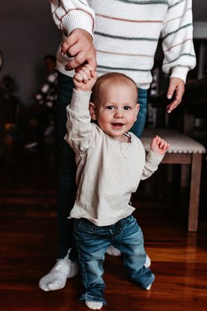 Small child in striped sweater and jeans taking first steps on hardwood floor.