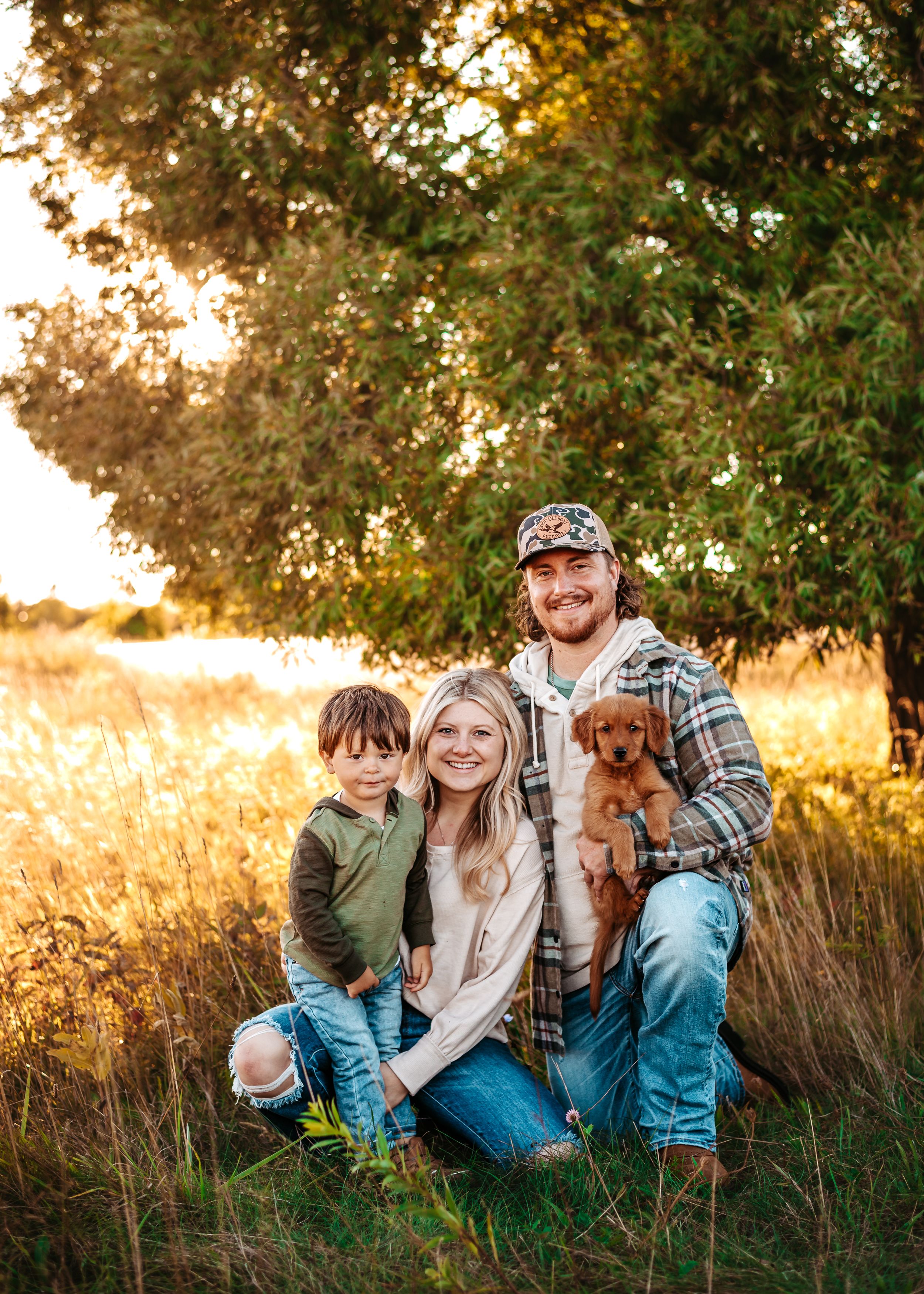 Family with small puppy posing together in golden sunset field.